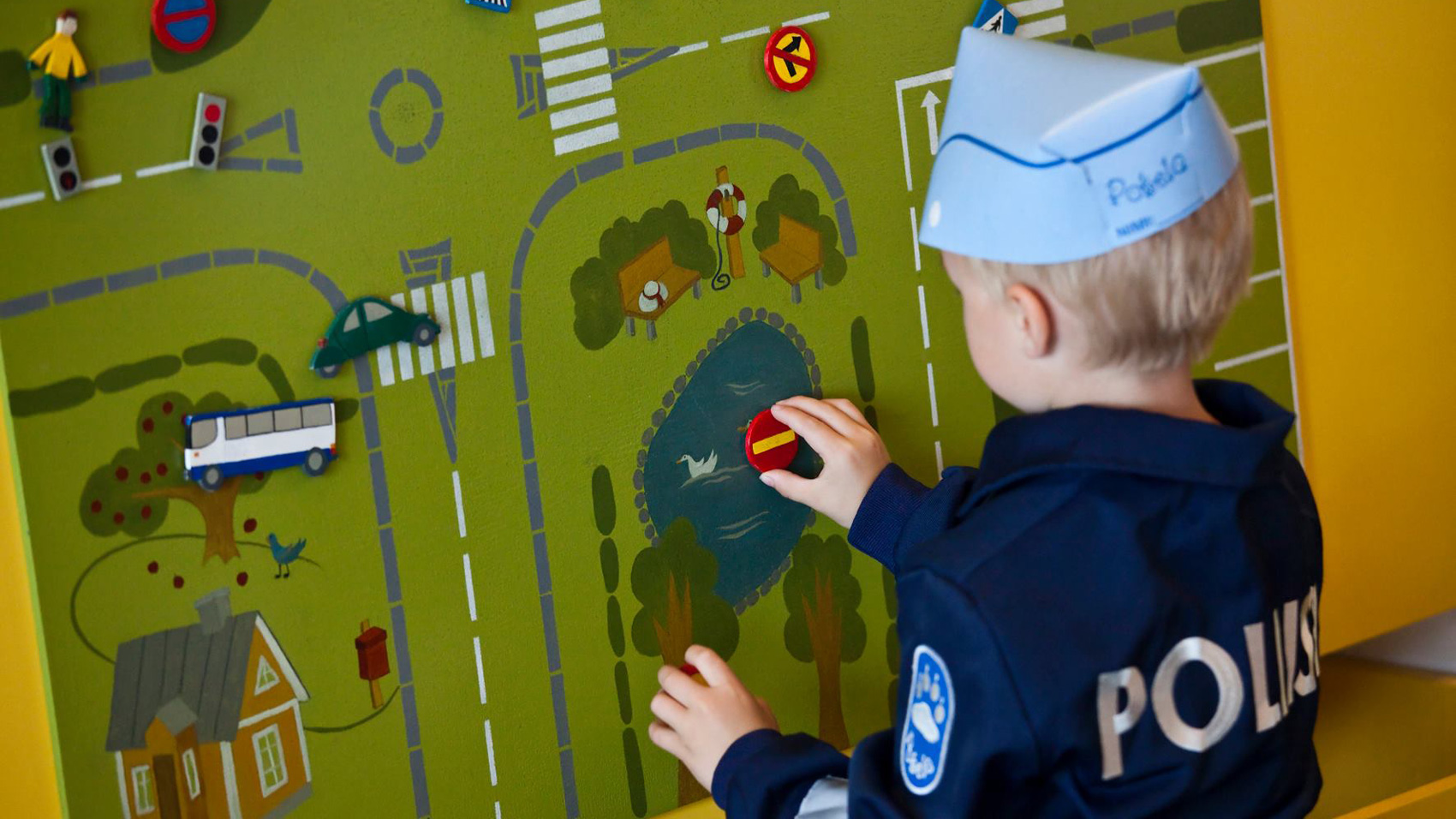 Lapsi leikkii Pokelassa liikenneleikkiä päällään poliisihaalari. Kuva Poliisimuseo.