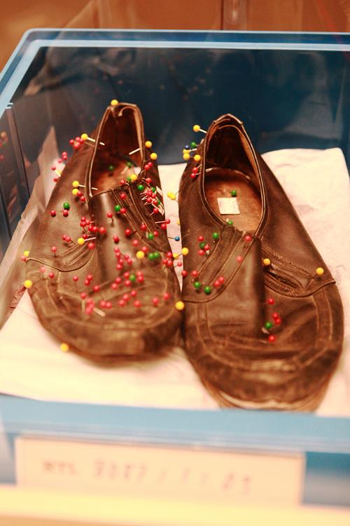 A pair of brown, wrinkled leather shoes with dozens of colorful pins stuck all over.