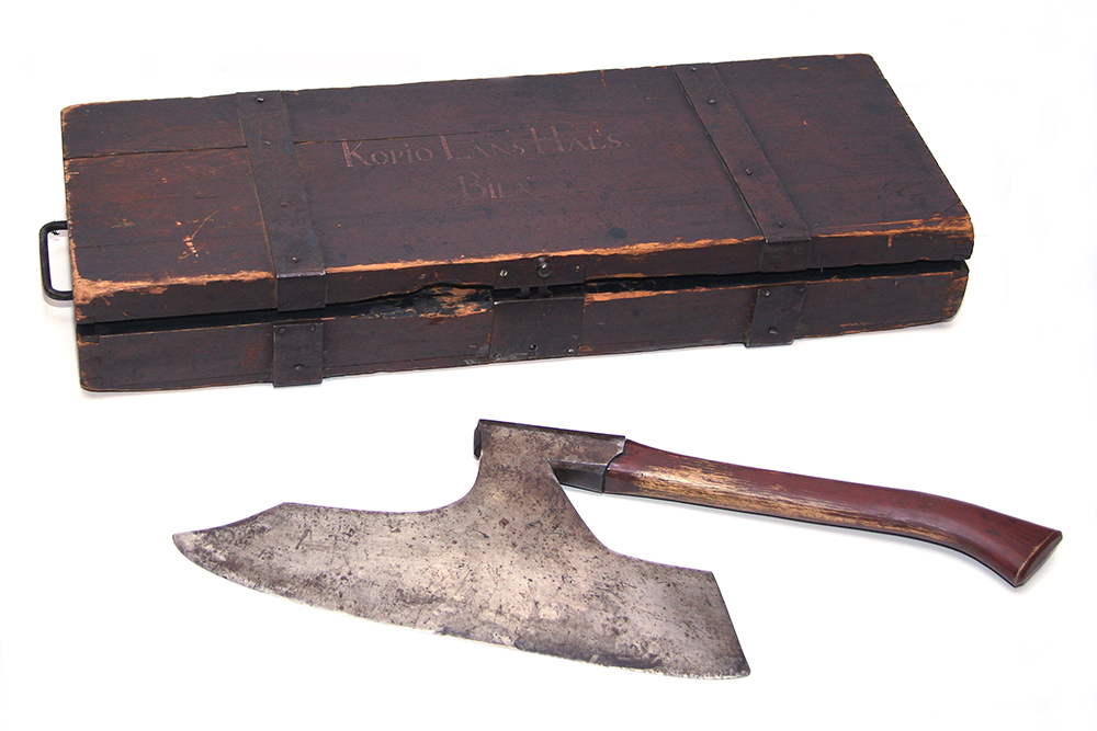 An axe with a wide blade and a wooden handle, behind the axe there is a wooden storage box.