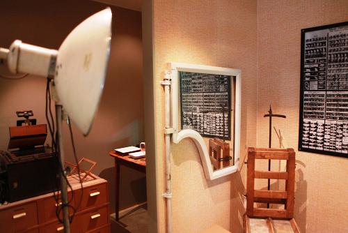 A wooden chair in which suspects were photographed for police records. At the front, there is a large lamp used when the photographs were taken. 