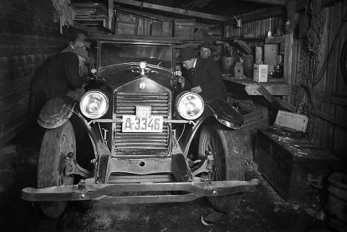 Mustavalkokuva, jossa neljä miestä tutkii autotallin sisällä olevaa autoa.