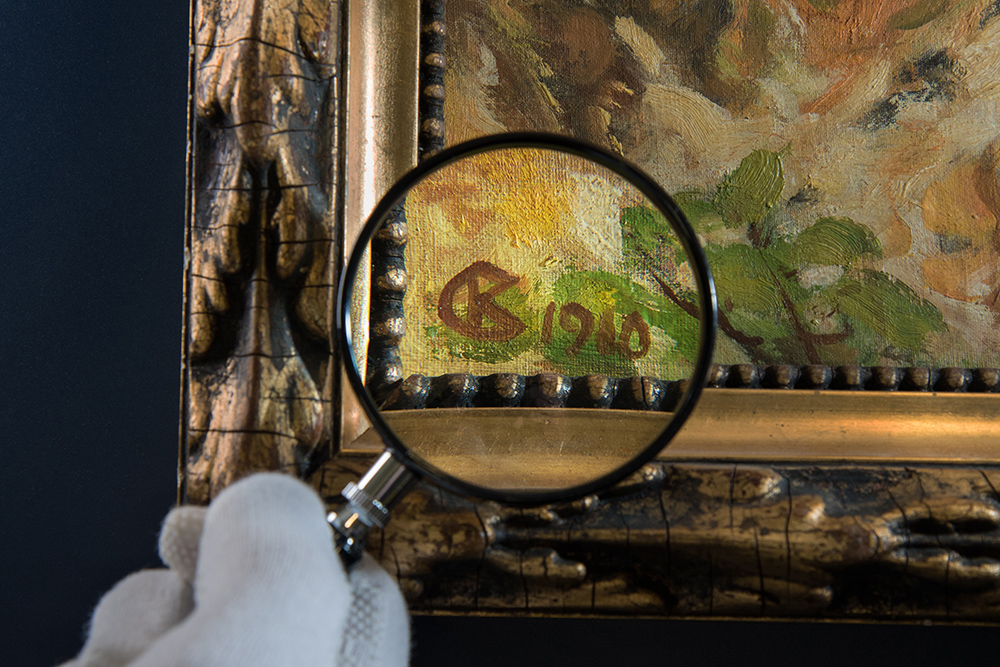A magnifying glass over a painting, the signature on the painting is being examined.