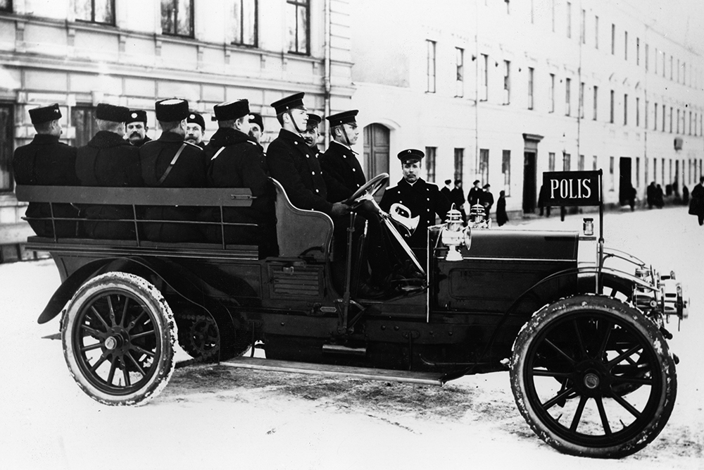 Old dark open top transport vehicle with ten officers on board.