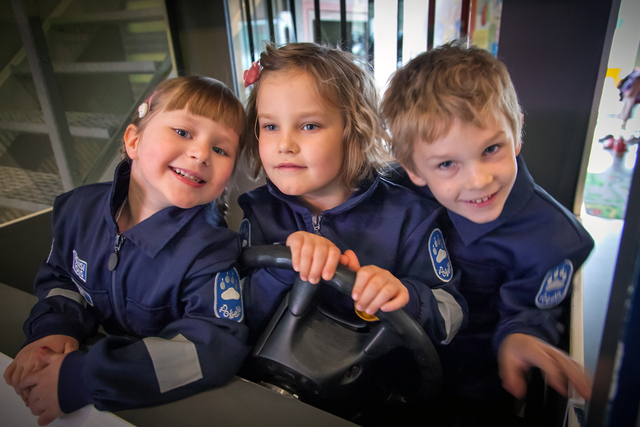 Three children wearing police overalls in Pokela, in the children’s own police car. Photo The Police Museum, Sami Hätönen.