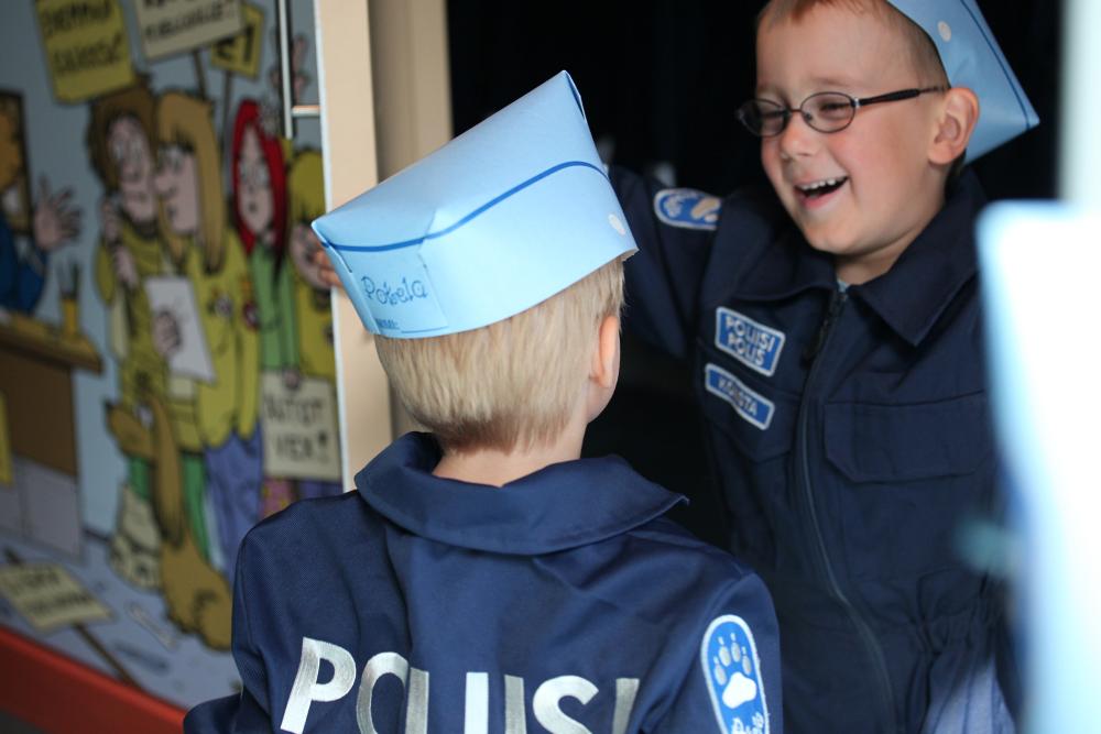 Two children in police overalls in Pokela, one with his back to the camera, the other one smiling.