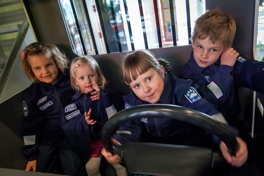 Fyra barn iklädda polisoveraller i barnens egen polisbil i Pokela.