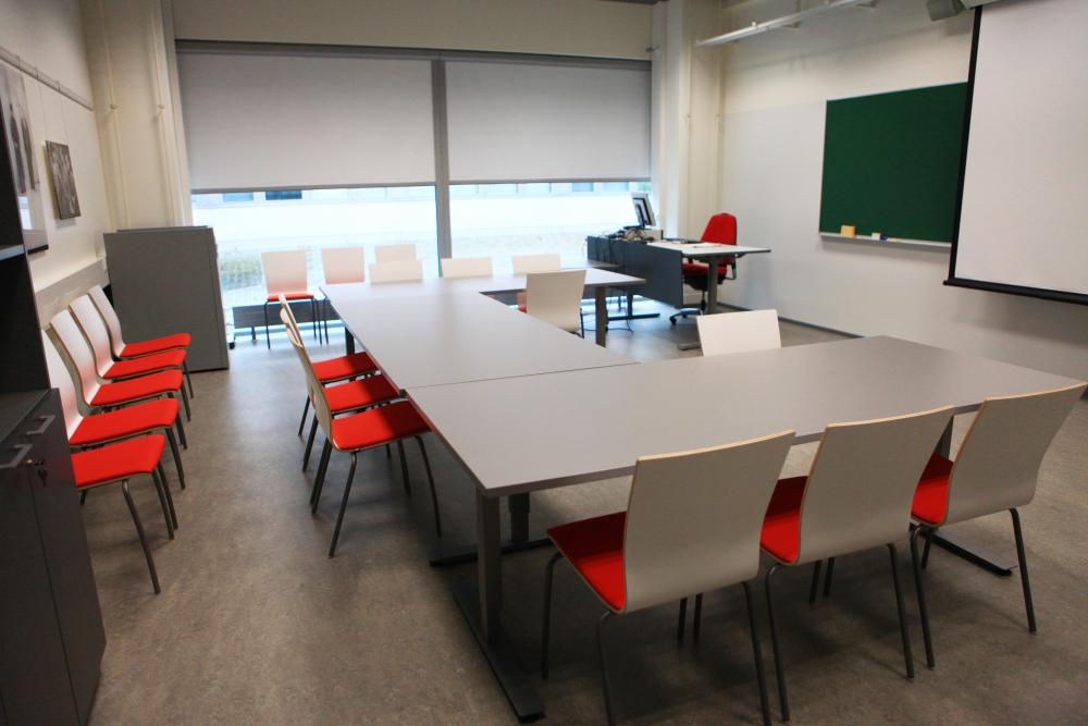 Tables and chairs in the museum's meeting room, a blackboard and a screen in the background.
