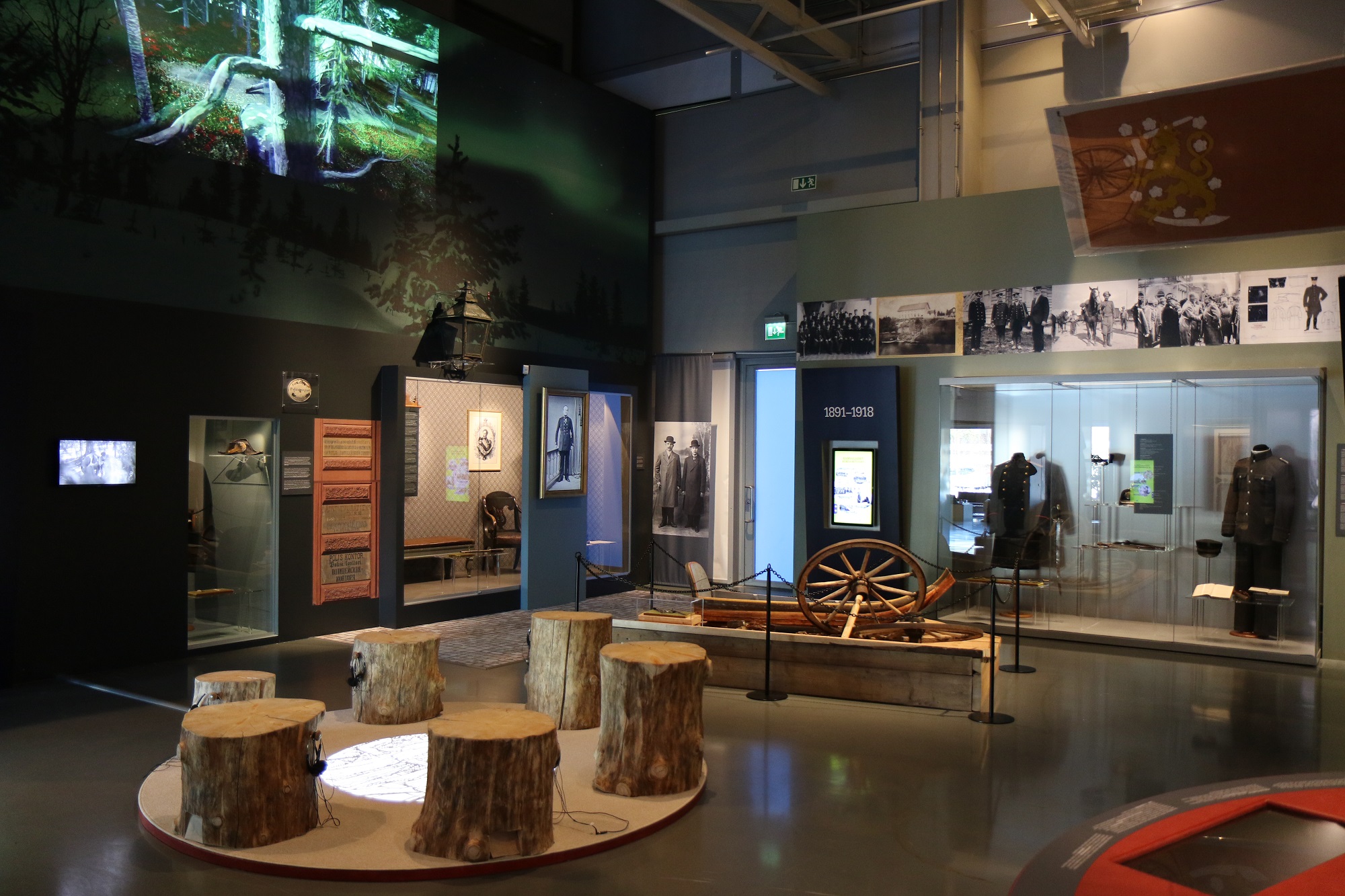 Bild av museets utställning. På bilden finns bland annat träbänkar för besökare och vitriner med utställningsföremål. Bild Polismuseet, Jarkko Järvinen