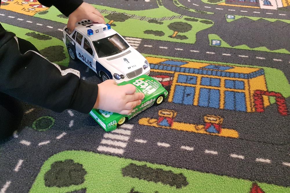 Ett barn leker med bilar på en matta med trafikmönster.