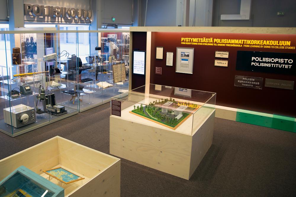 General view of the exhibition “Formally Qualified – A century of Finnish police education”. The picture shows, among others, a scale model, a Police School sign on the wall and old objects in a showcase.